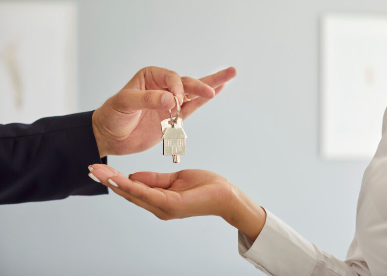 Close up of realtor handing keys to young woman from new home representing property purchase or rent